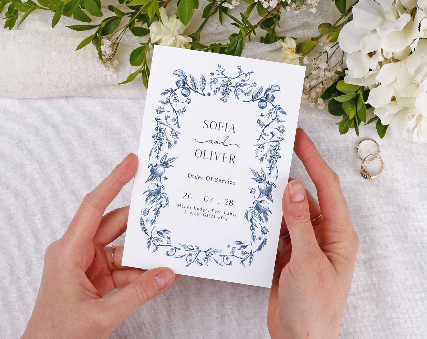 Blue Garden Order Of Service booklet held in hands featuring floral design and names for wedding ceremony.