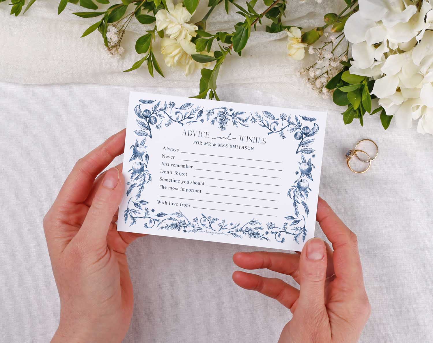 Hands holding a Blue Garden Wedding Advice Cards on a table with floral decor.