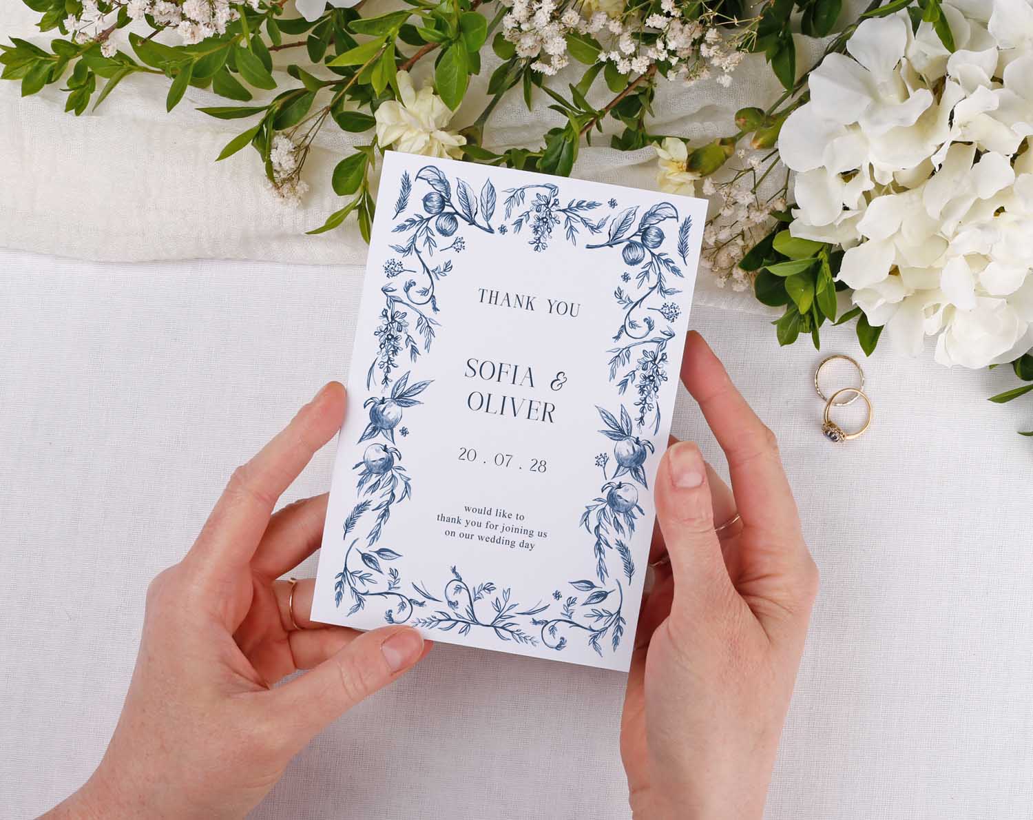 Person holding Blue Garden Wedding Thank You Cards surrounded by greenery and floral decorations.