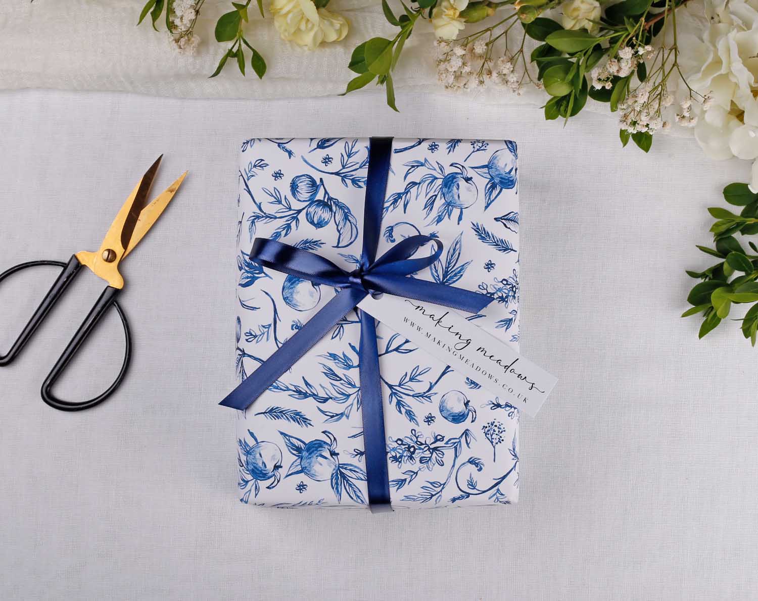 Blue Garden Wedding Wrapping Paper with navy ribbon and scissors on a table surrounded by flowers.