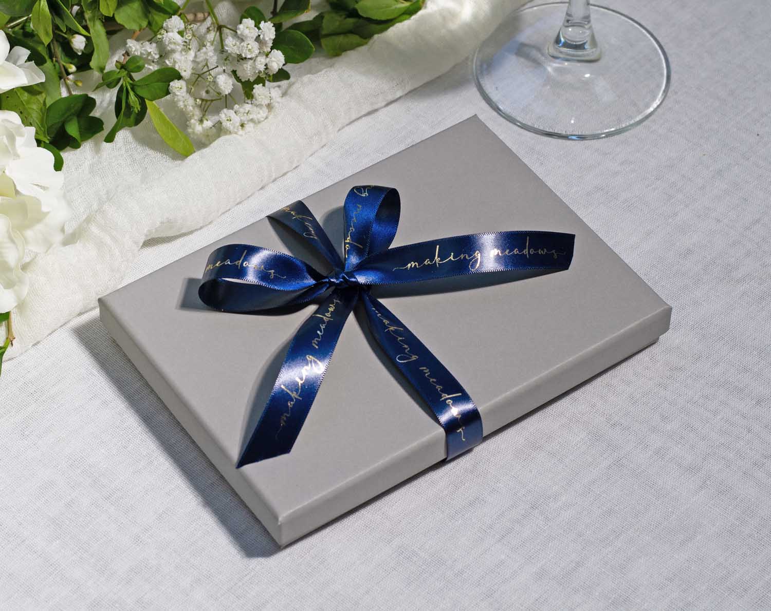 Boho Wedding Table Game gift box with a blue ribbon on a table with flowers and a glass.