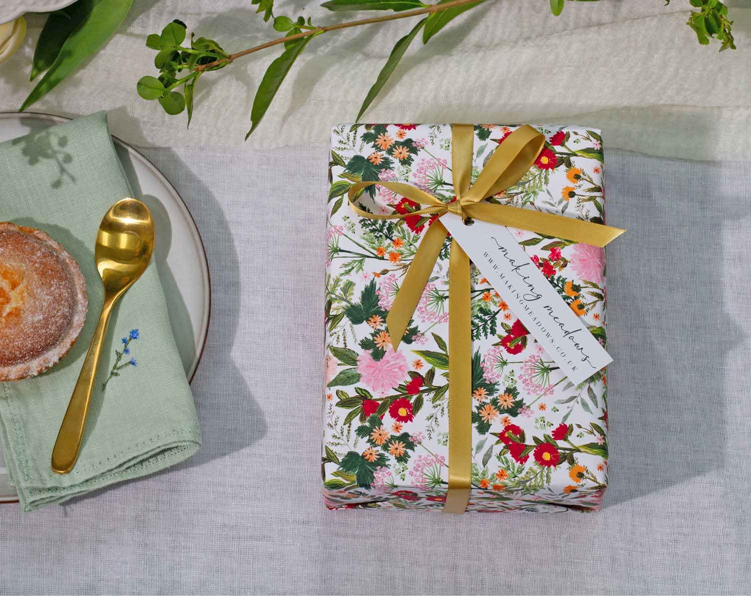 Boho Wedding Wrapping Paper elegantly wrapping a gift with vibrant floral design and gold ribbon on a table.