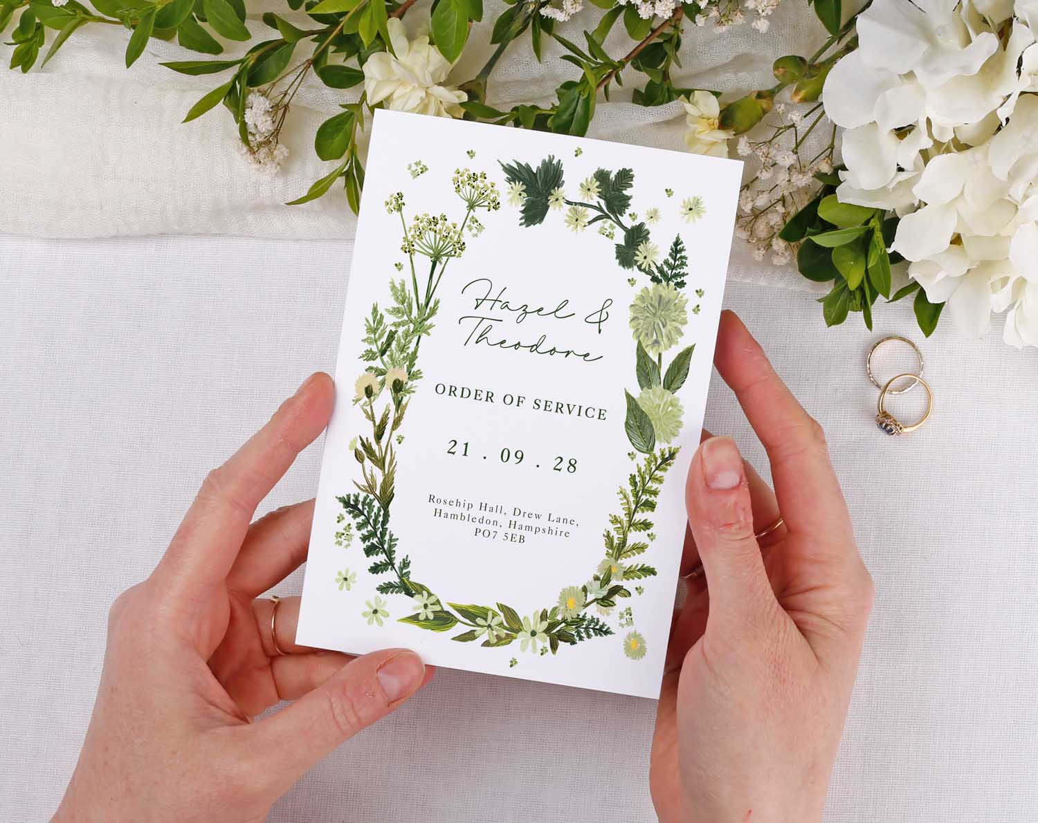 Botanical Order Of Service booklet held by hands, featuring greenery and floral design for wedding ceremony.