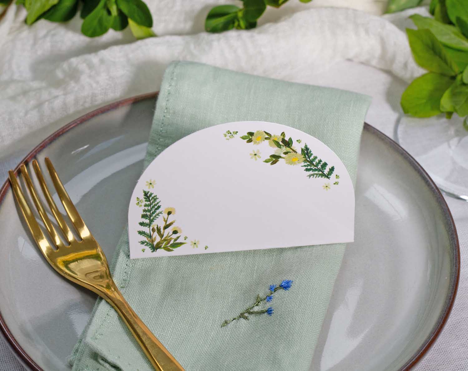 Botanical Wedding Place Cards displayed on a green napkin with a gold fork, featuring lush greenery designs.