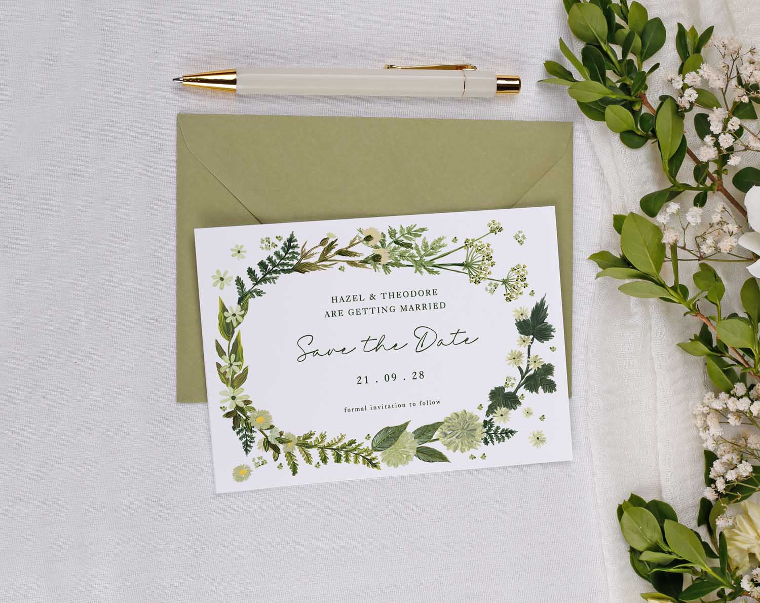 Botanical Wedding Save The Date card featuring greenery design, envelope and pen on a white table.
