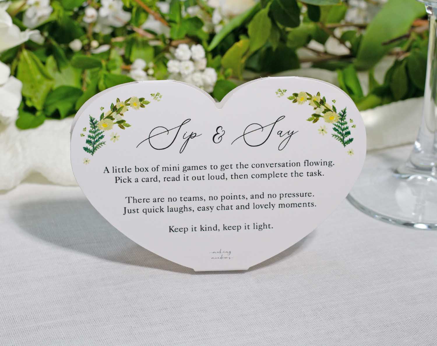 Botanical Wedding Table Game featuring a heart-shaped card with "Sip & Say" written on it, designed for wedding table interaction.