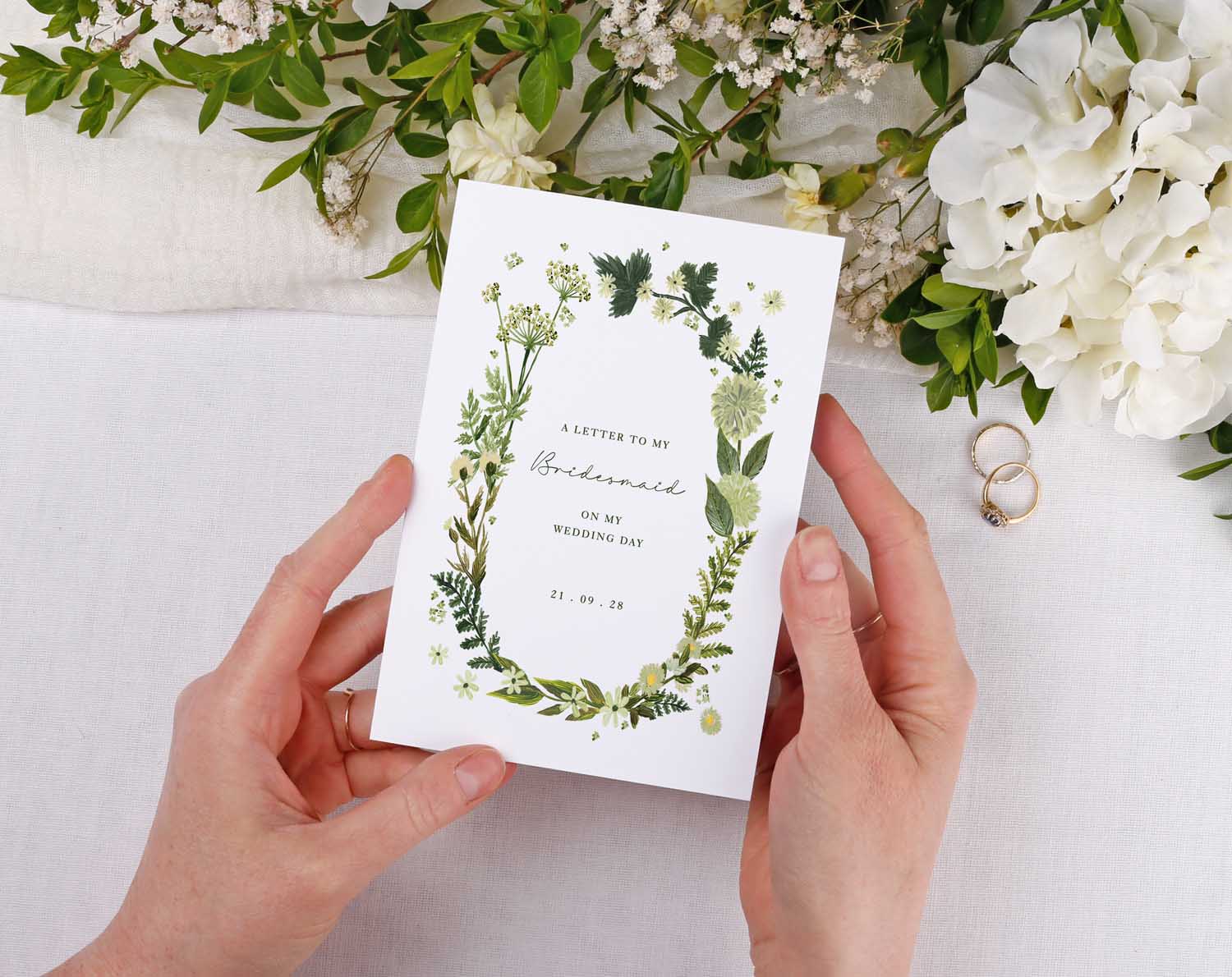 Botanical Wedding Thank You Card held in hands with floral design and rings in the background.