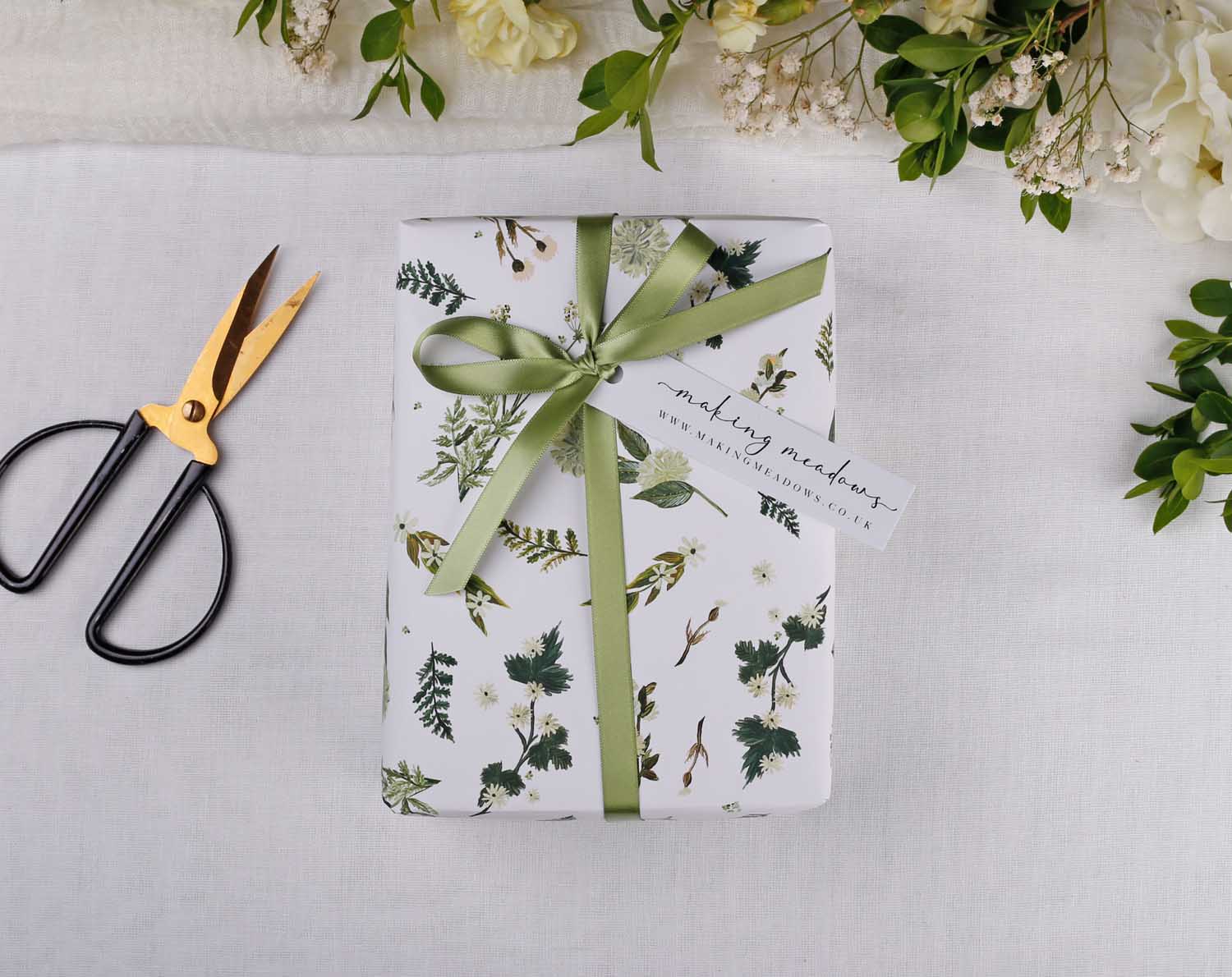 Botanical Wedding Wrapping Paper beautifully wrapped with green ribbon and tag, surrounded by floral decor and scissors.