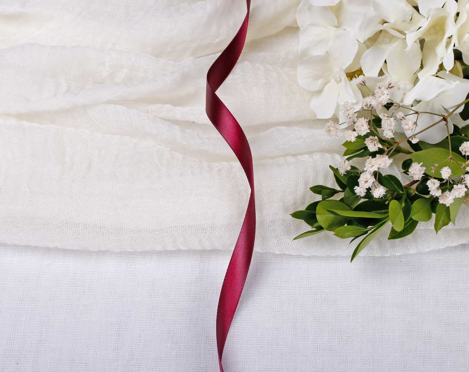 Burgundy Red Satin Ribbon For Wedding elegantly featured beside floral arrangements on a white fabric surface.