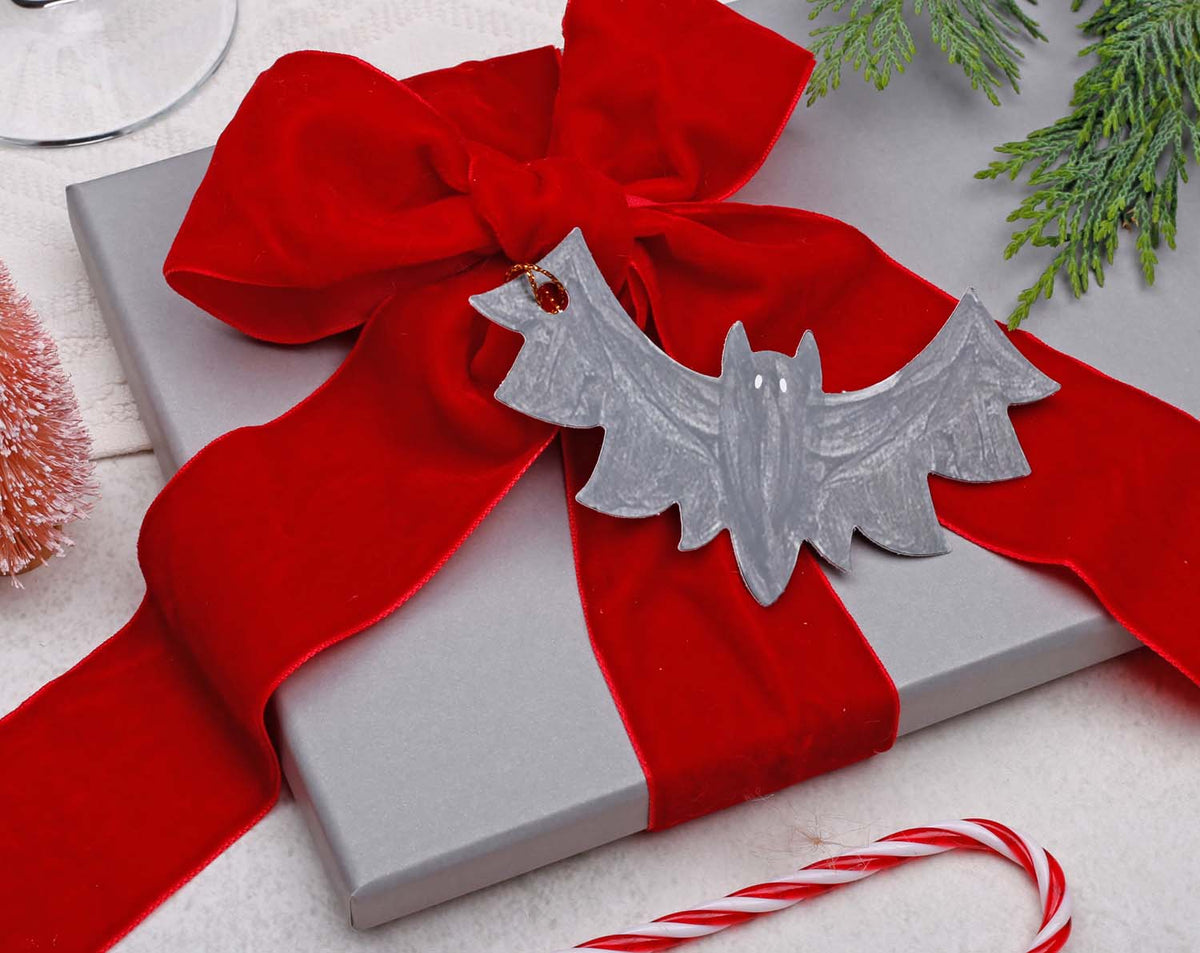 Bat Christmas Gift Tags attached to a wrapped gift with a red bow and holiday decorations.