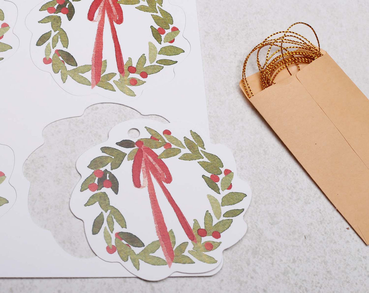 Wreath Christmas Gift Tags featuring floral designs with red ribbons and brown kraft envelopes.