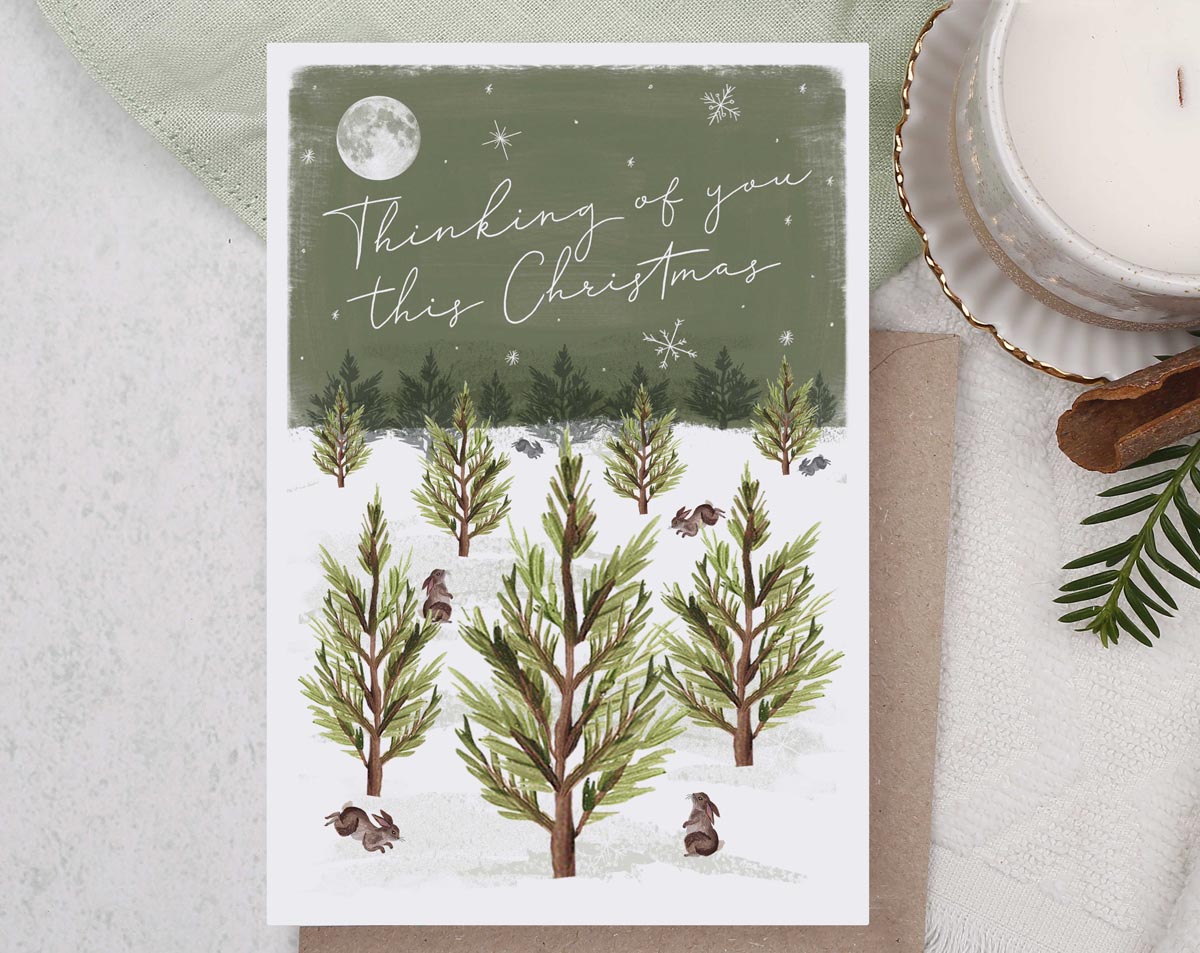 Thinking of You Christmas card, illustrated with a festive deer and robin, snow filled forest with foliage and mushrooms galore. 