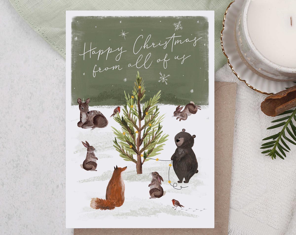 Christmas card, illustrated with a family of woodland animals and a snow filled forest with foliage and trees