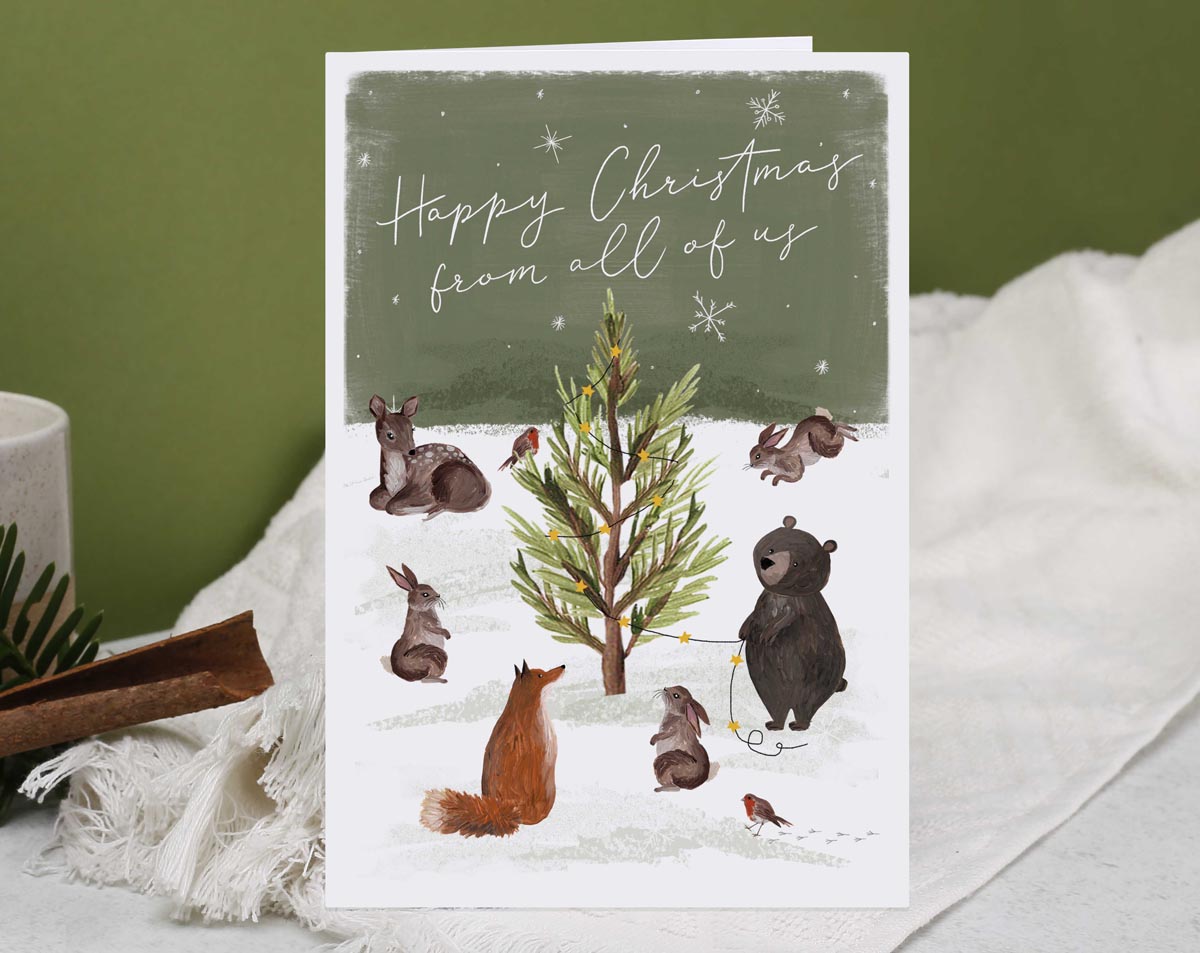 Christmas card, illustrated with a family of woodland animals and a snow filled forest with foliage and trees
