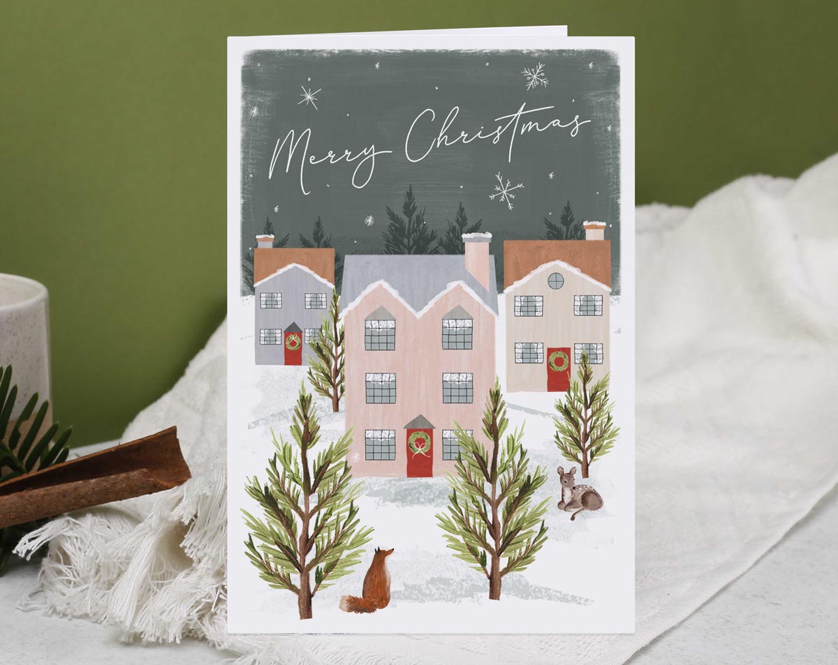 Christmas card, illustrated with a snowy village of houses and a cute fox in the woods.