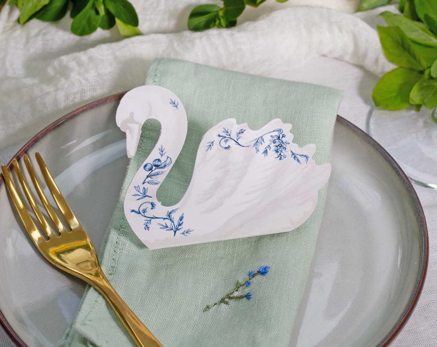 Floral Swan Wedding Place Cards on a green napkin next to a fork, enhancing a wedding table setting.