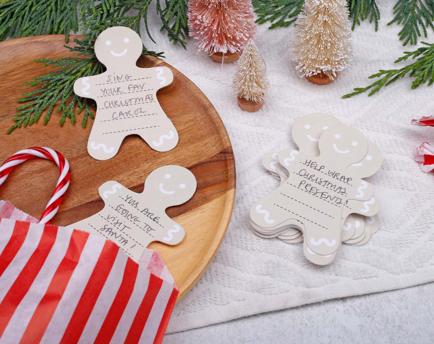 Gingerbread Fill Your Own Activity Cards on a wooden platter surrounded by festive decor and a gift bag.