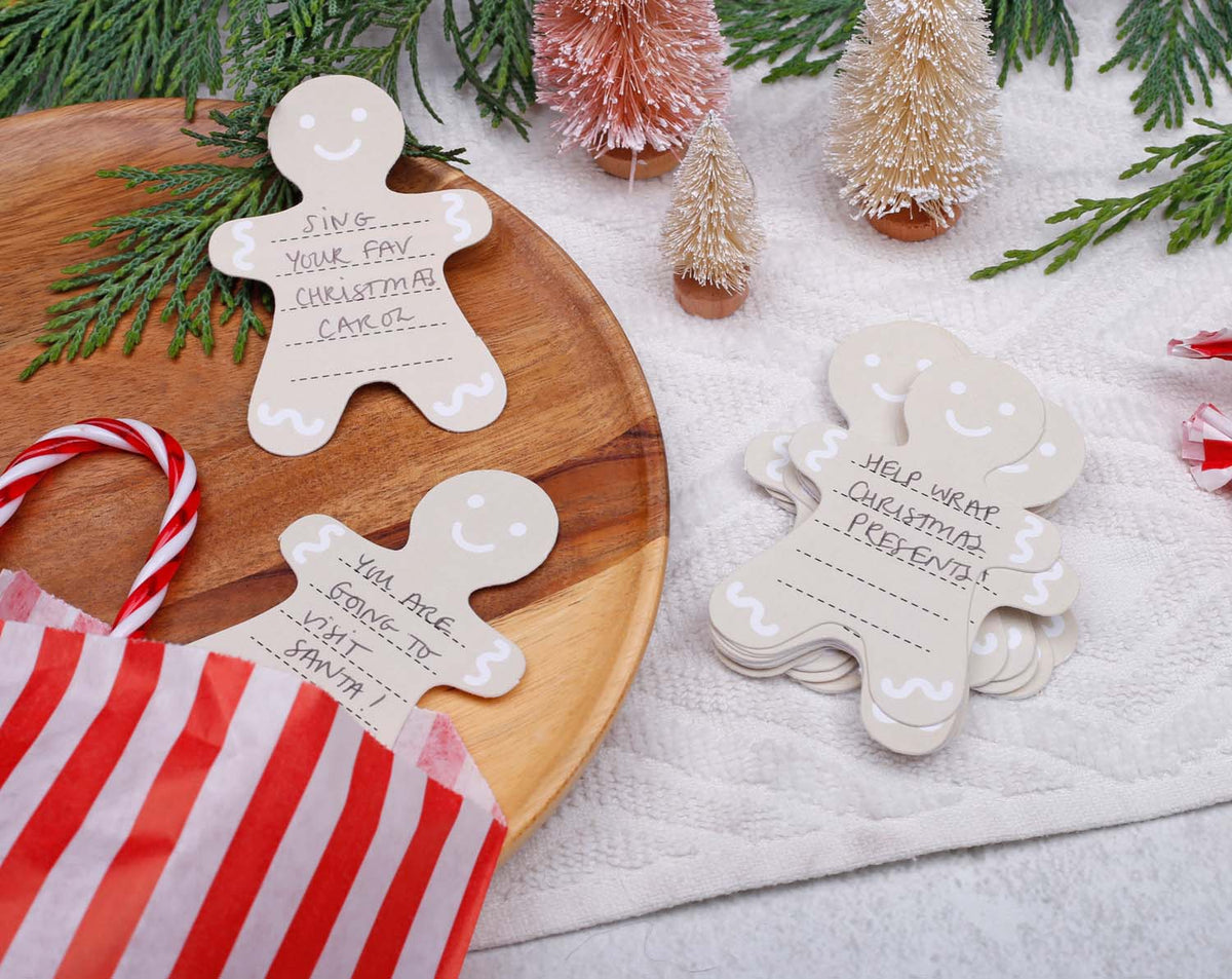 Gingerbread Fill Your Own Activity Cards on a wooden platter surrounded by festive decor and a gift bag.