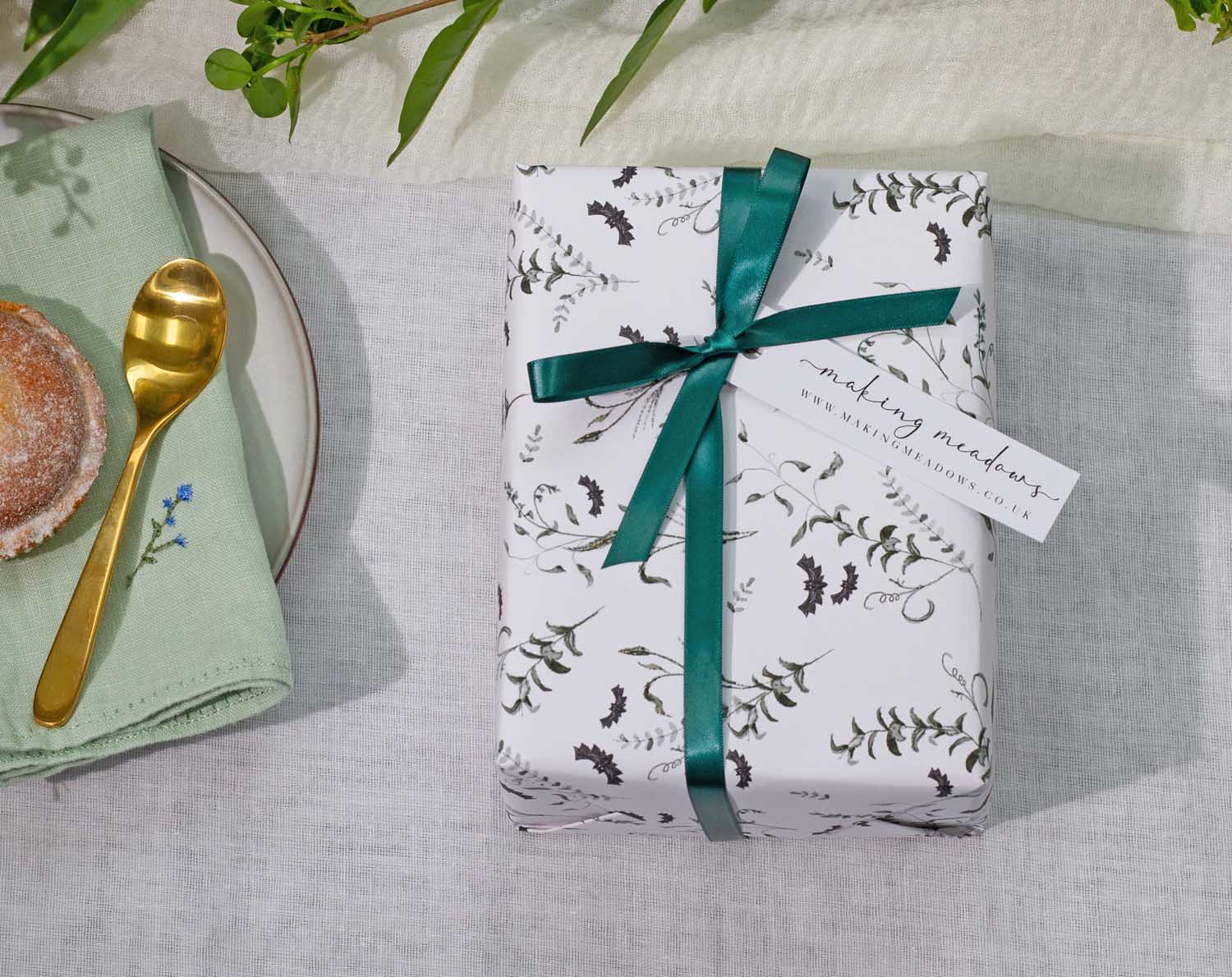 Gothic Wedding Wrapping Paper elegantly wrapped gift with green ribbon and tag on a dining table.