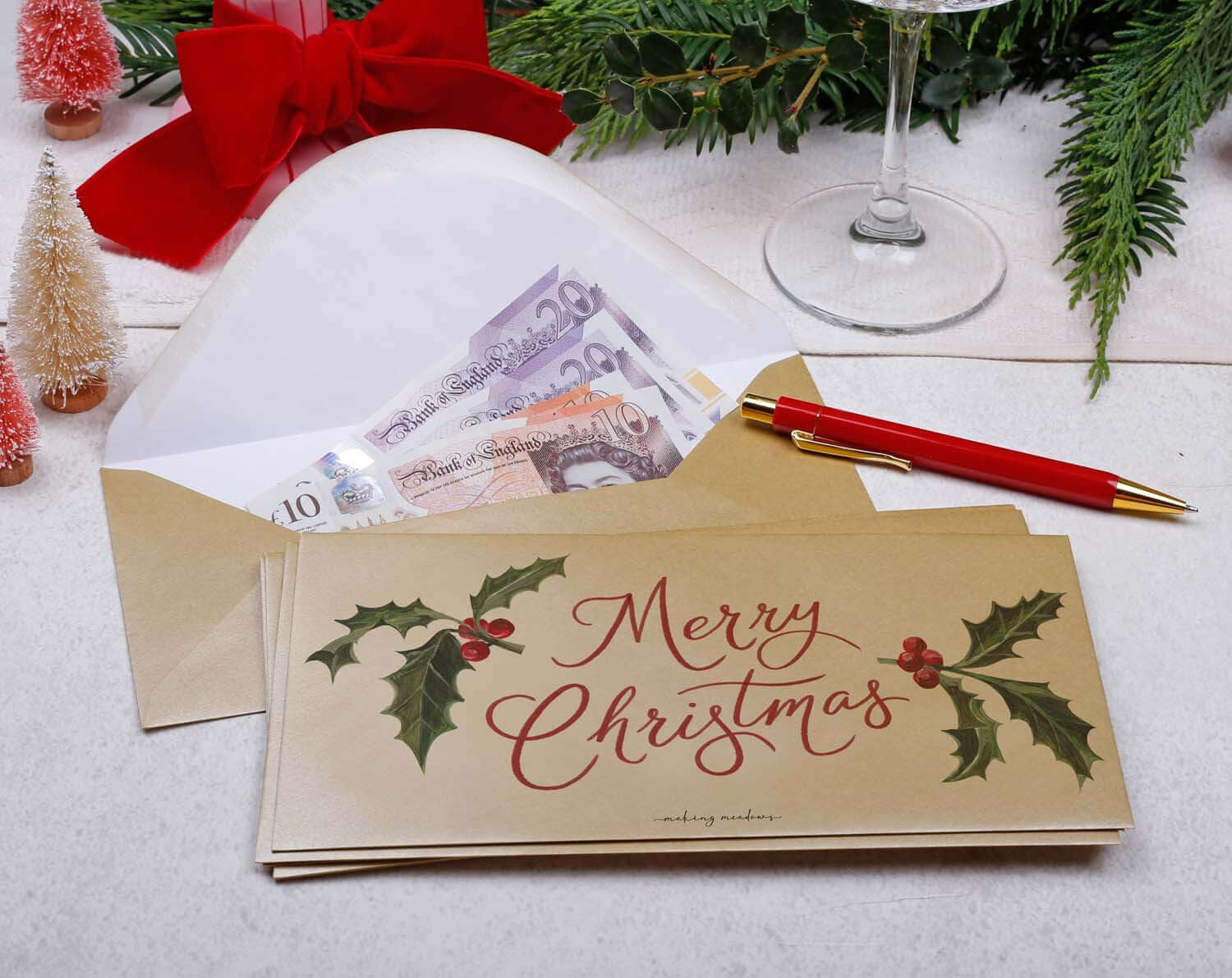 Holly Christmas Money Envelopes featuring festive designs, nestled with cash and a pen for holiday gift giving.