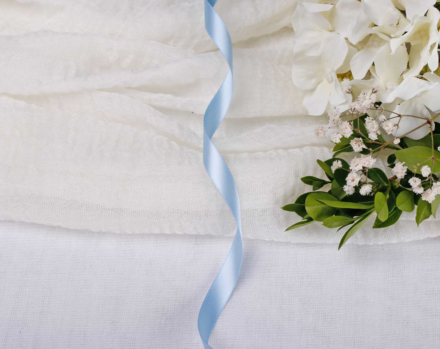 Light Blue Satin Ribbon For Wedding on white fabric with flowers and greenery, ideal for elegant wedding decorations.