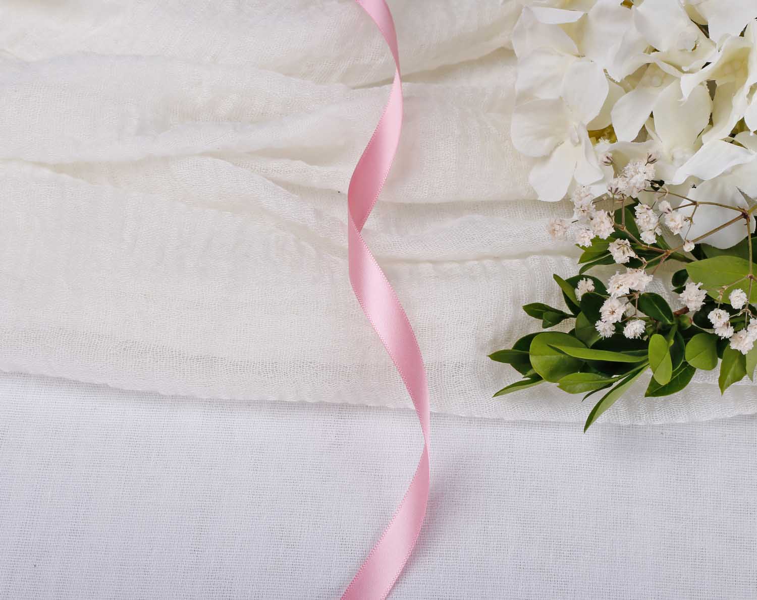 Light Pink Satin Ribbon For Wedding over white fabric with flowers in the background, perfect for wedding stationery.