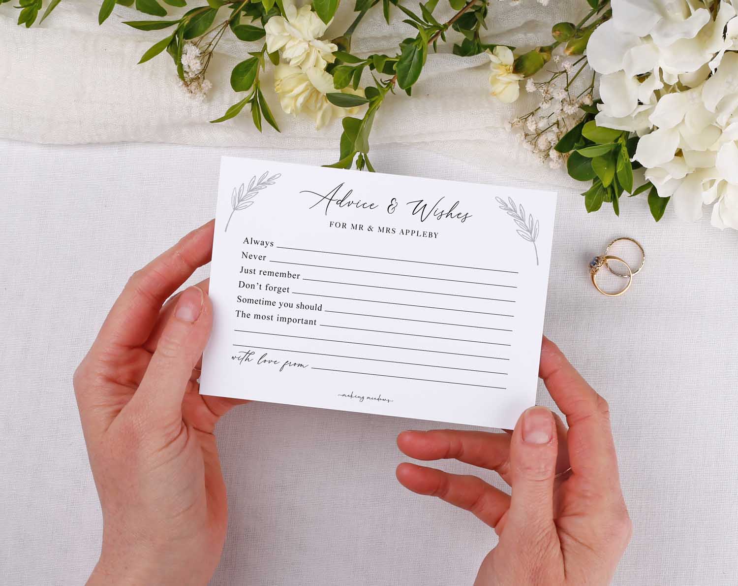 Minimalist Wedding Advice Cards held by hands with floral decor and wedding rings in the background.