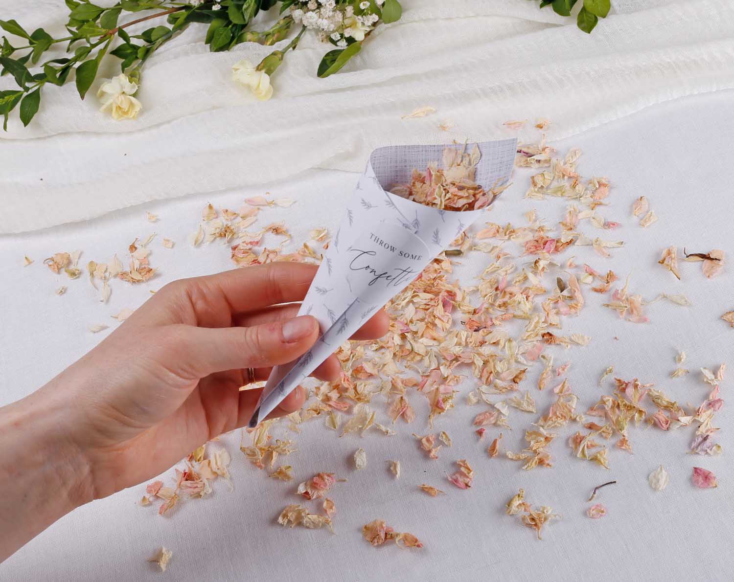 Minimalist Wedding Confetti Cones held in hand with dried flower petals scattered on a table.