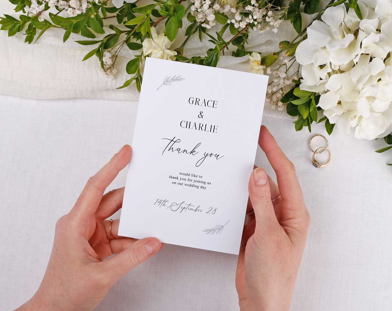 Minimalist Wedding Thank You Cards displayed in hands surrounded by flowers and wedding rings.