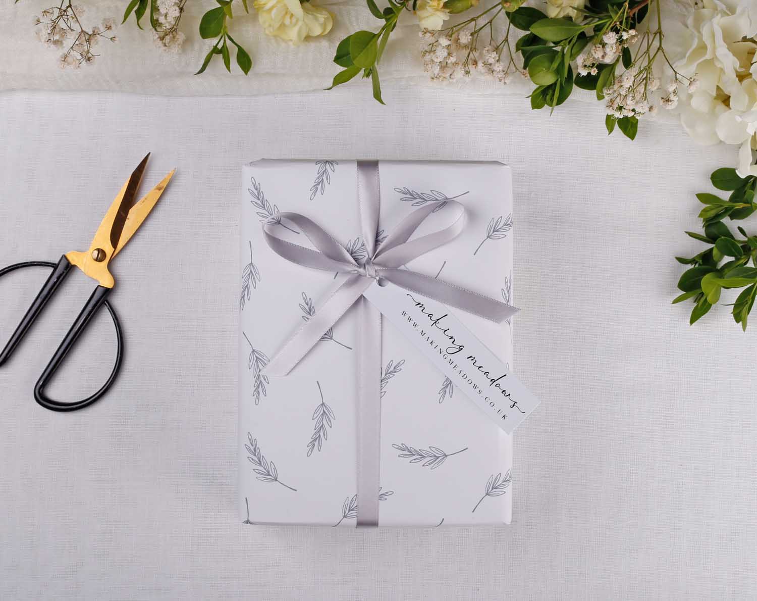 Minimalist Wedding Wrapping Paper gift wrapped with a ribbon and tag, surrounded by floral decorations and scissors.