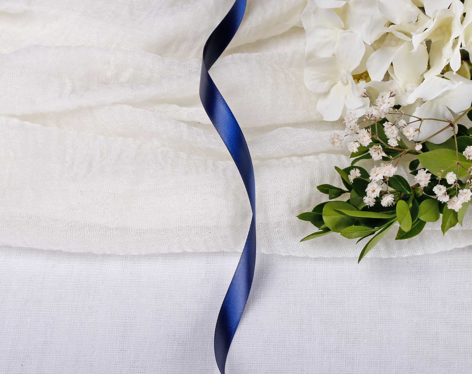 Navy Blue Satin Ribbon For Wedding laid on white fabric with flowers, perfect for wedding stationery decoration.