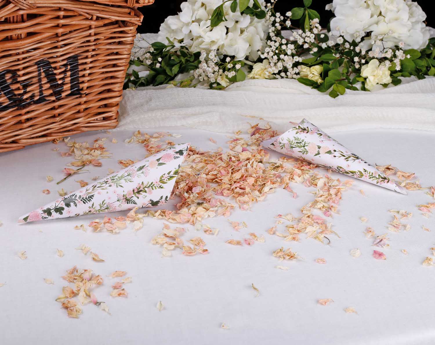 Pink Floral Wedding Confetti Cones on a table with dried petals and a wicker basket for wedding ceremony.
