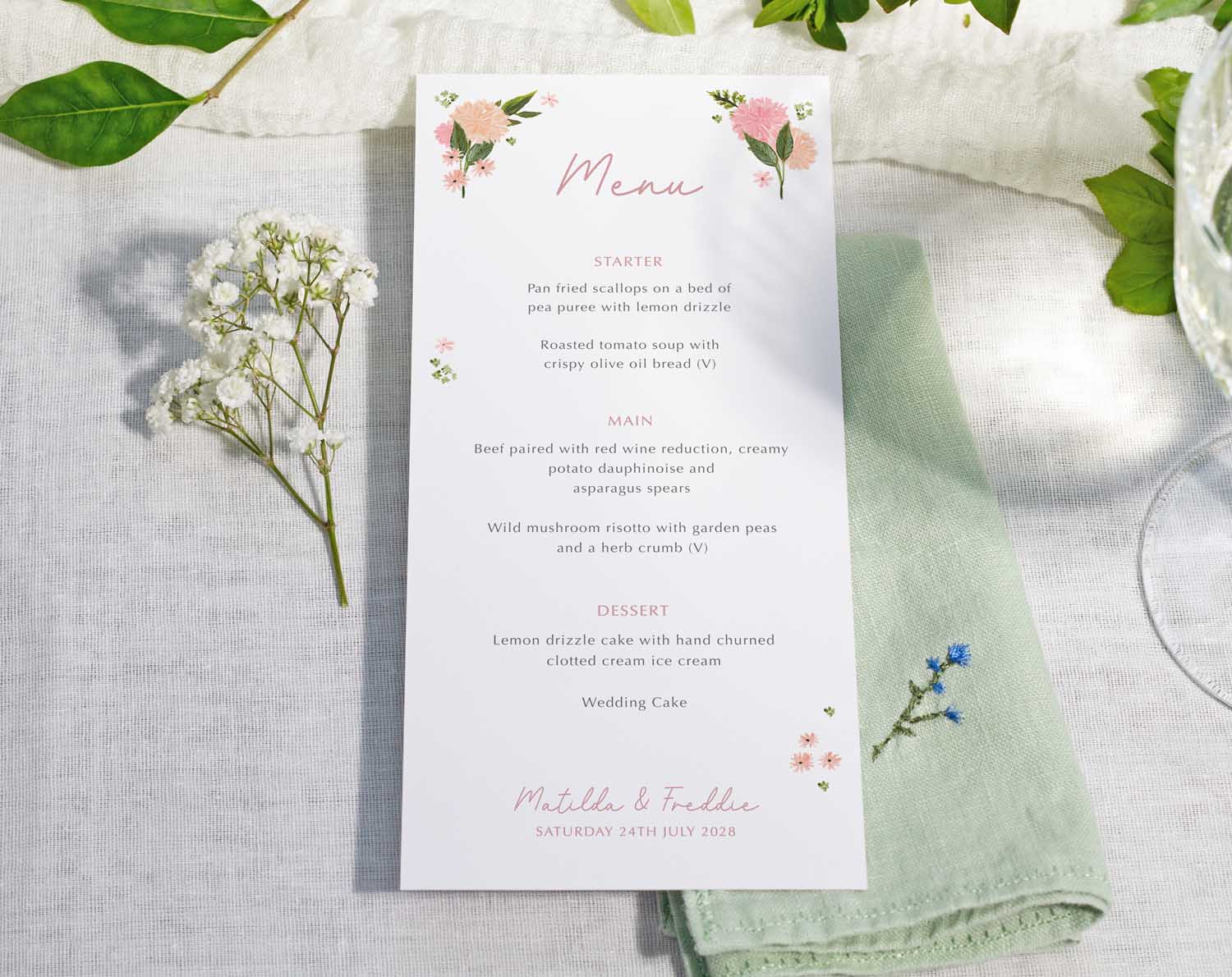 Pink Floral Wedding Menus displayed on a table with fresh greenery and a vintage napkin.