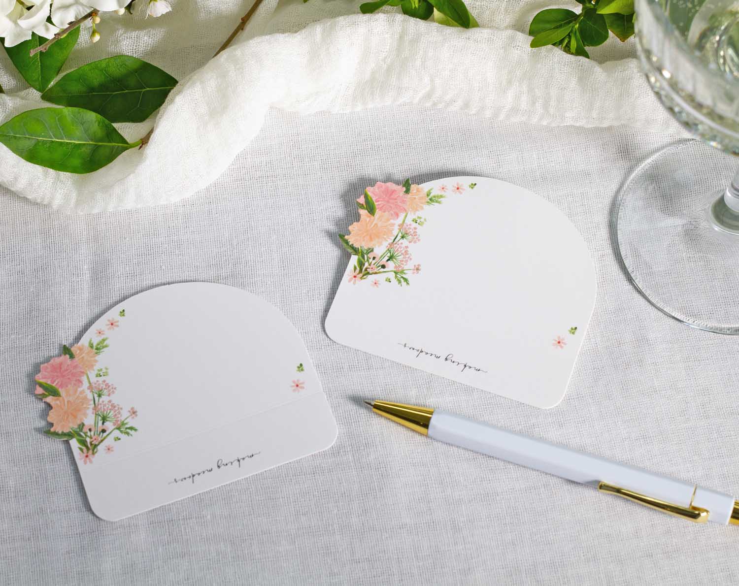 Pink Floral Wedding Place Cards on a table with greenery and a pen, perfect for elegant seating arrangements.
