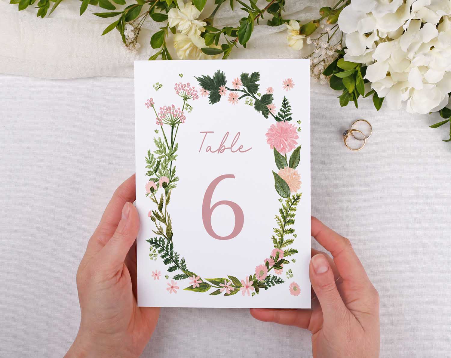 Pink Floral Wedding Table Numbers displayed for Table 6 with floral design and elegant hands holding it.