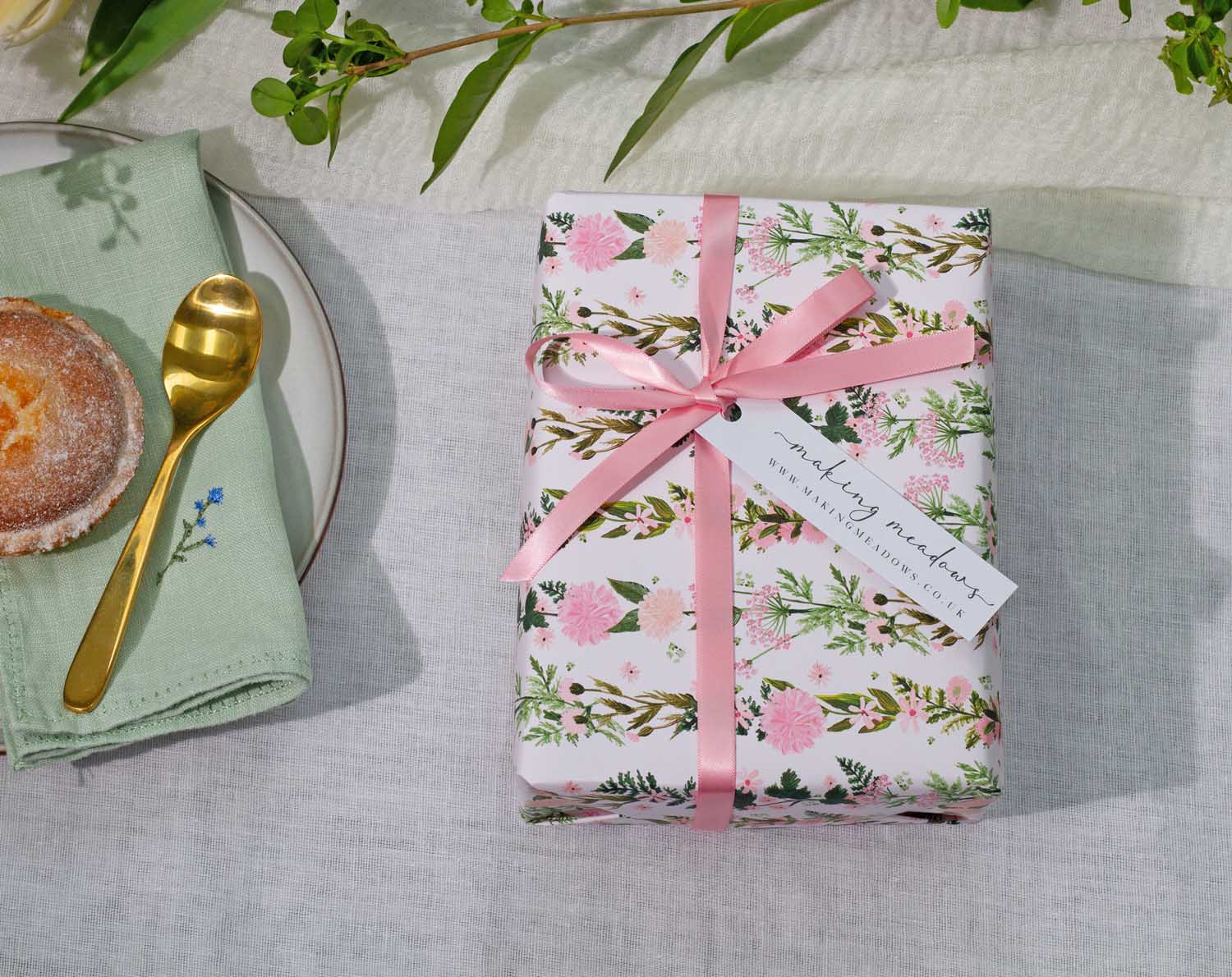 Beautifully wrapped gift using Pink Floral Wedding Wrapping Paper and pink ribbon on a dining table setting.