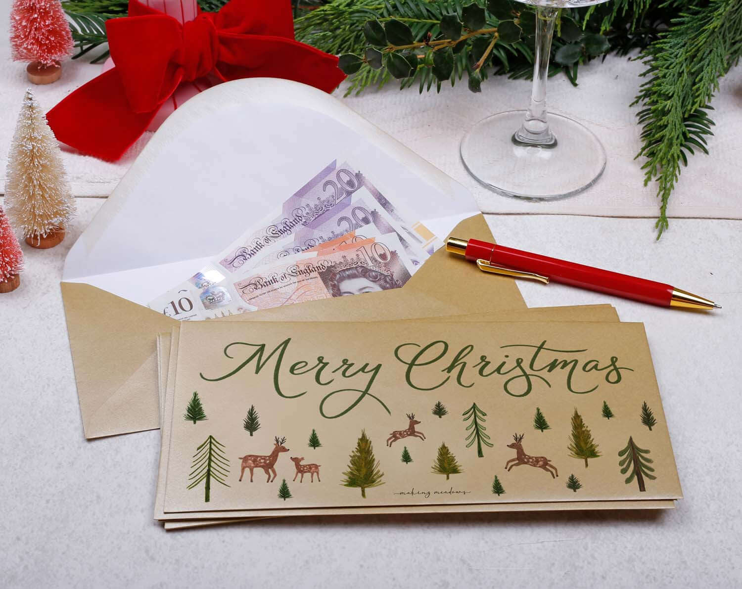 Reindeer Christmas Money Envelopes featuring festive illustration and cash inside with a red pen and holiday decor.