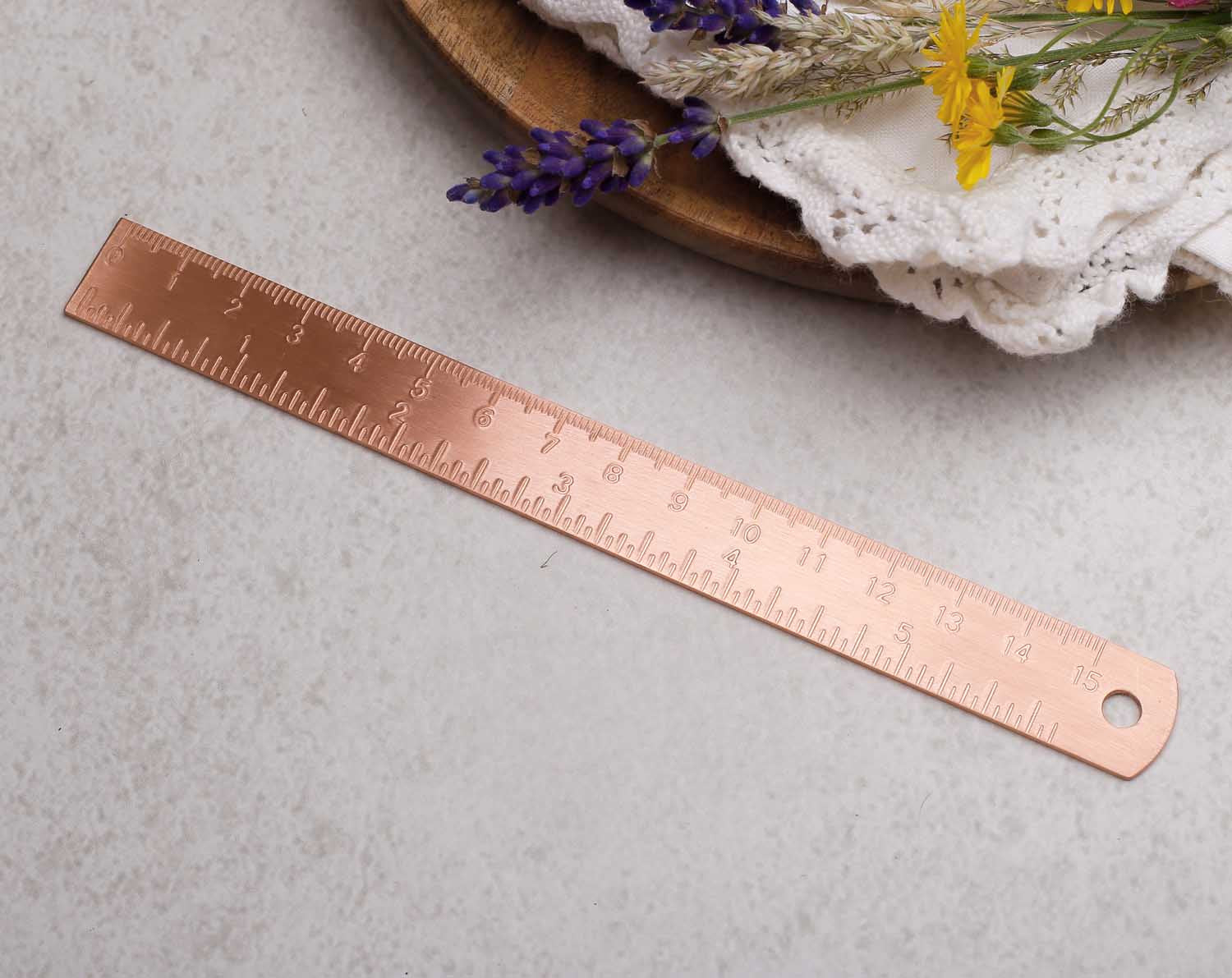 Copper ruler on a textured surface with flowers in the background