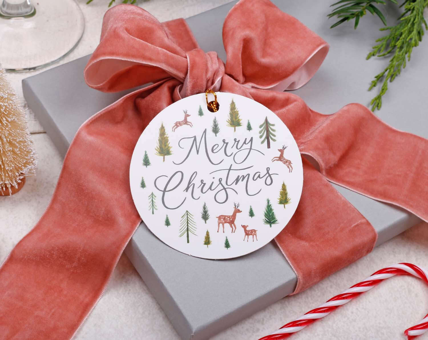 Rustic Christmas Gift Tags on a gift wrapped with pink velvet ribbon, featuring forest illustrations and Merry Christmas message.