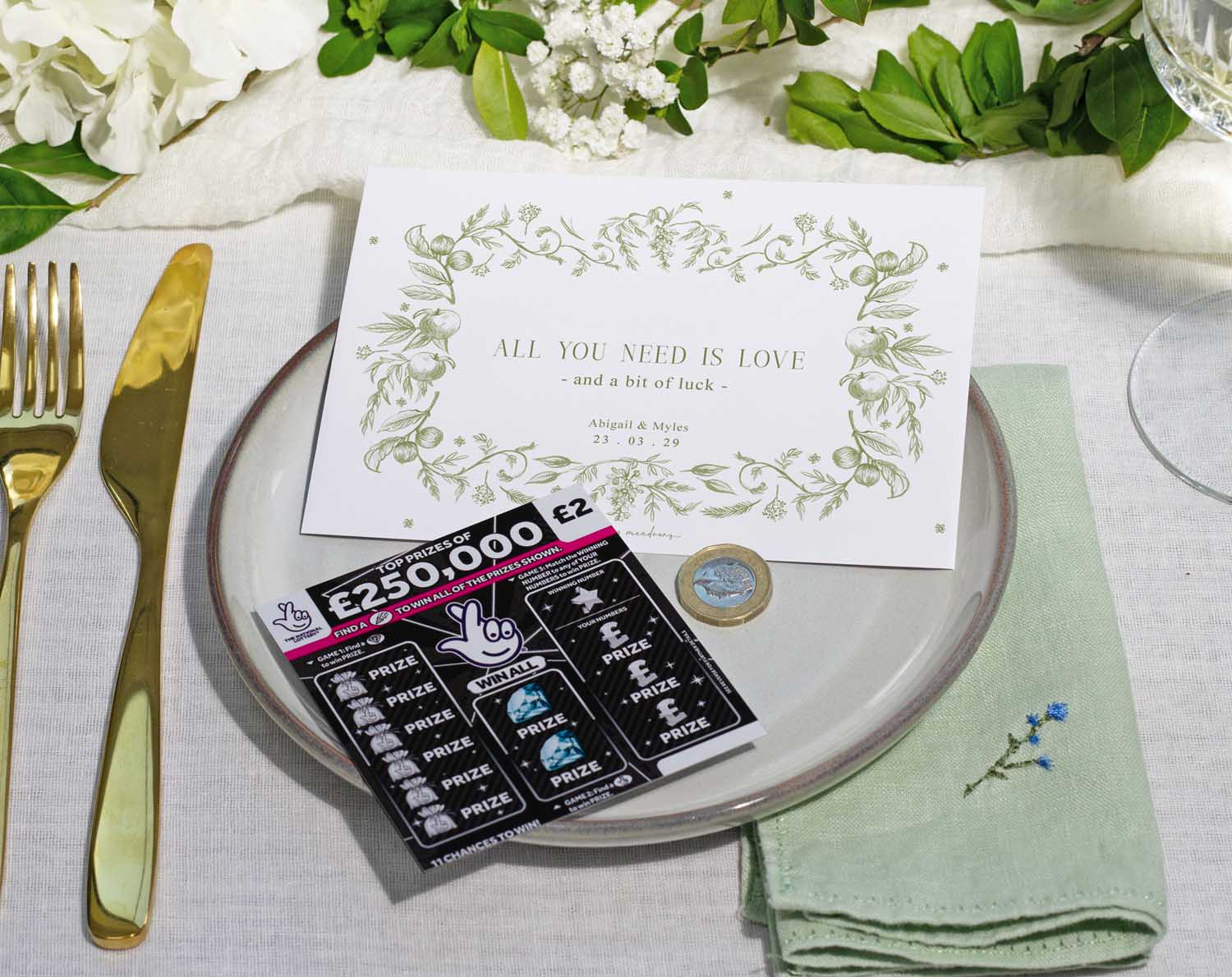 Sage Garden Scratch Card Envelopes displayed on a wedding table setting with cutlery and floral decor.