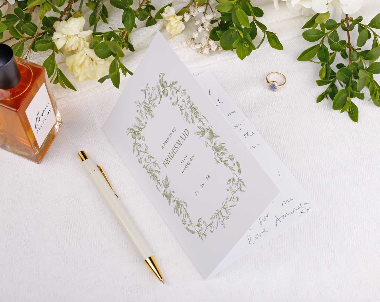 Sage Garden Wedding Thank You Card displayed with flowers and a ring on a table beside a perfume and pen.