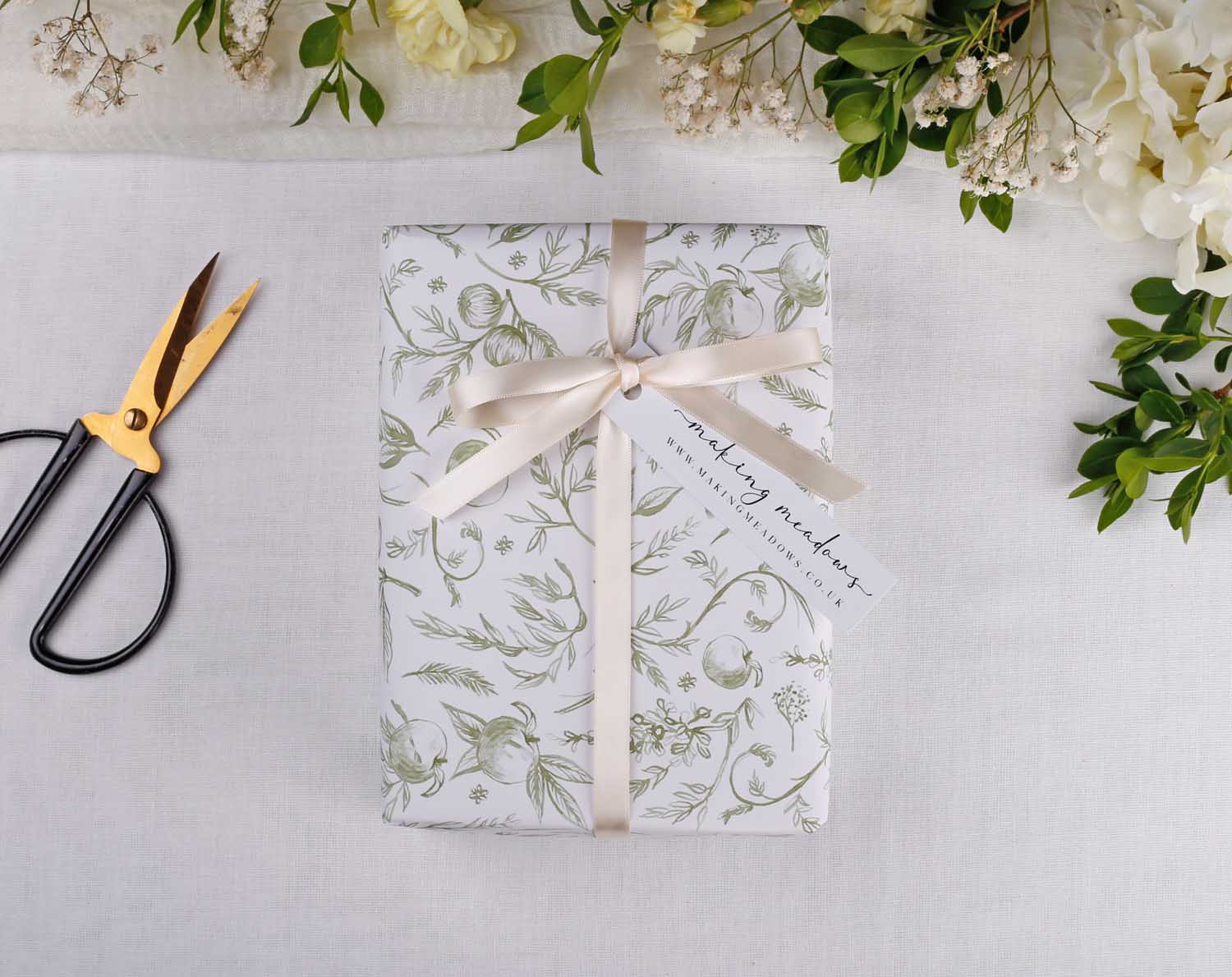 Sage Garden Wedding Wrapping Paper elegantly wraps a gift, adorned with a ribbon and tag, showcasing floral design.