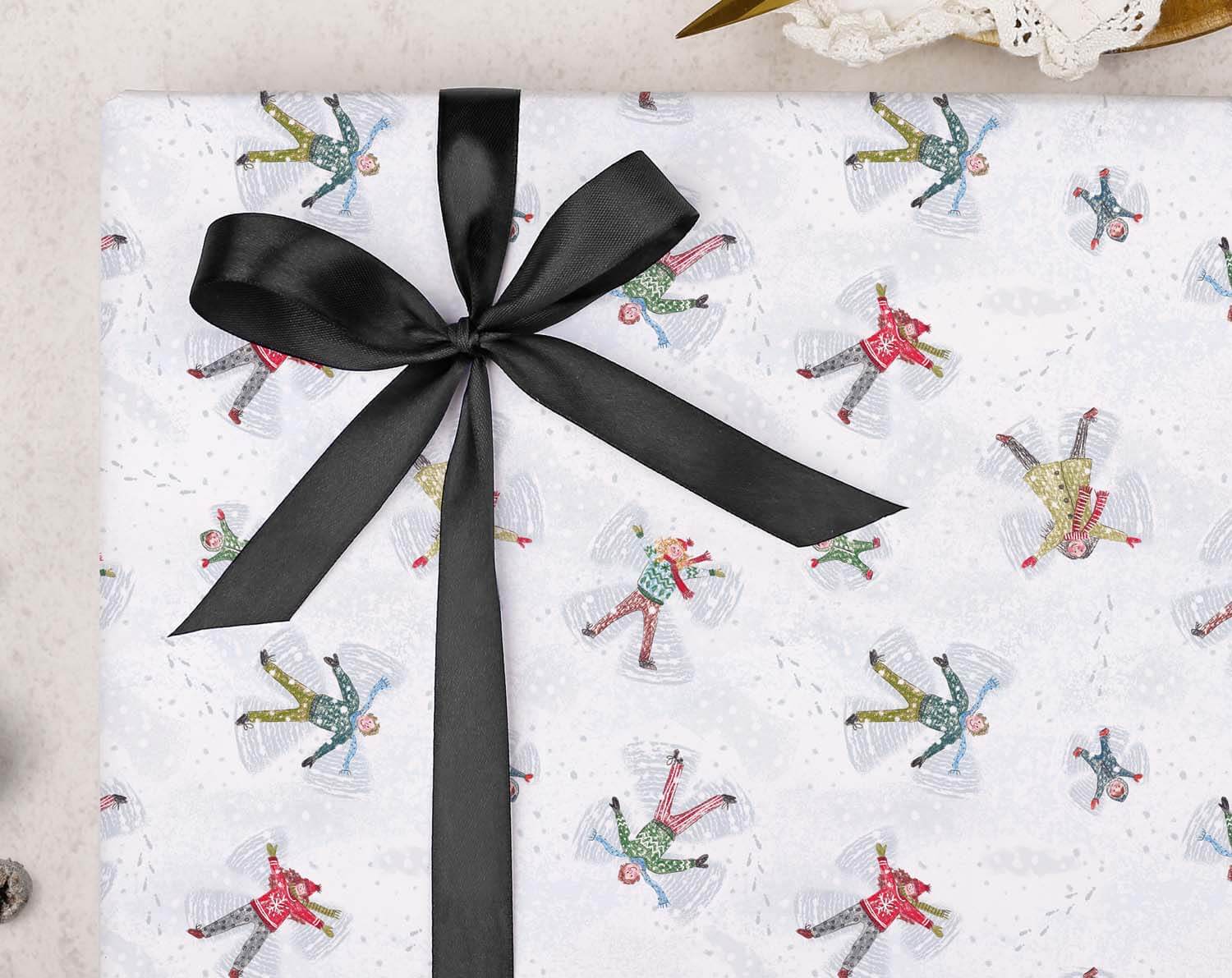 Snow Angels Christmas Wrapping Paper featuring snow angel designs and a black ribbon bow.