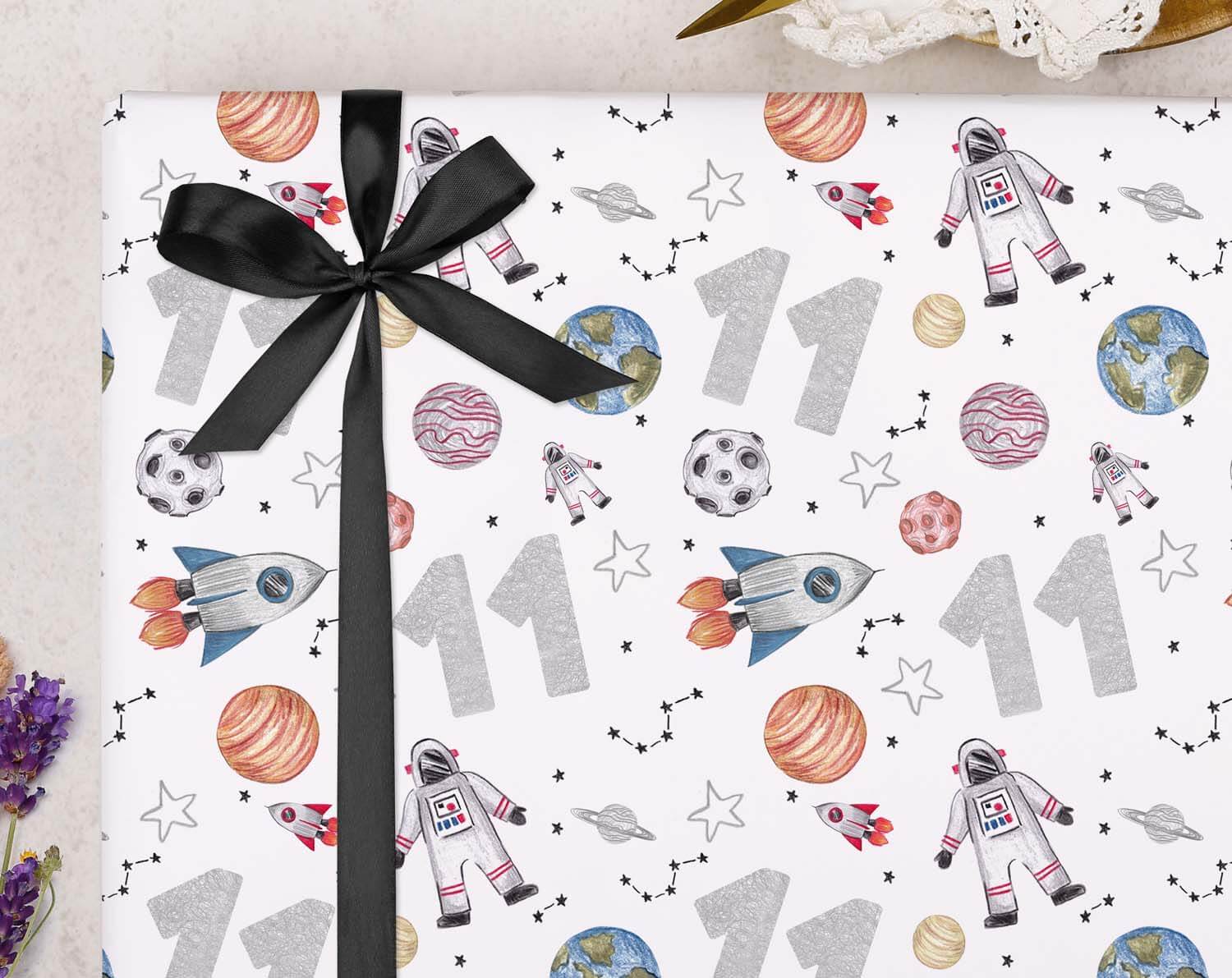 Space 11th Birthday Wrapping Paper with colorful space theme, rockets, planets, and number 11, tied with a black ribbon.