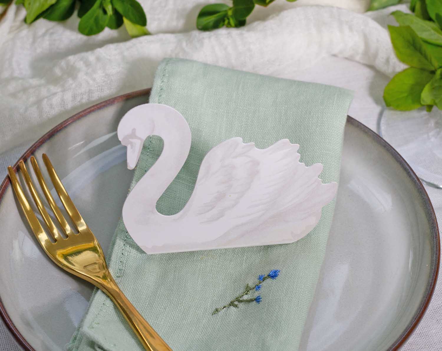 Swan Wedding Place Cards on a green napkin beside a gold fork, adding elegance to wedding table settings.