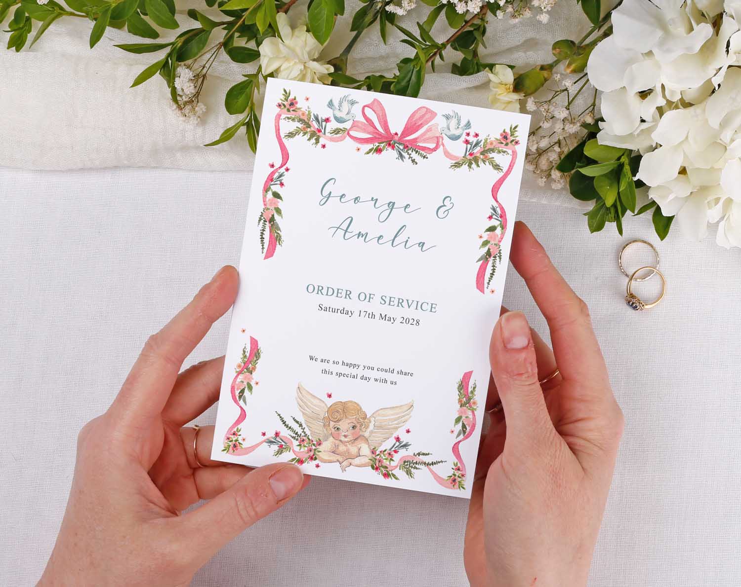 Vintage Order Of Service booklet held by hands, featuring floral design and cherub illustration for a wedding ceremony.