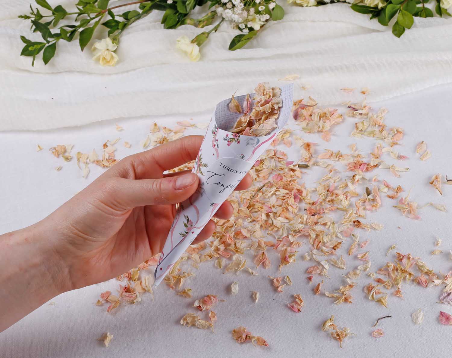 Vintage Wedding Confetti Cones held in hand with flower petals scattered on a table, perfect for wedding ceremonies.
