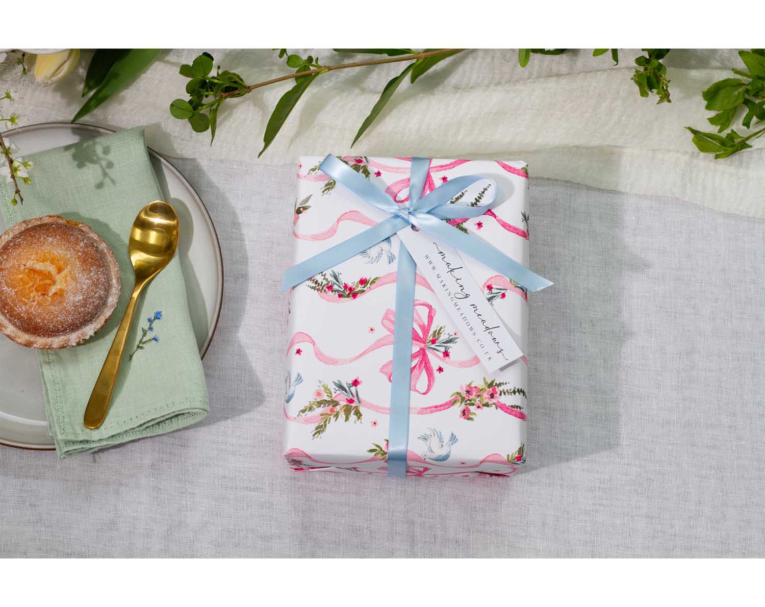 Beautifully wrapped gift using Vintage Wedding Wrapping Paper with floral designs and a blue ribbon on a table setting.