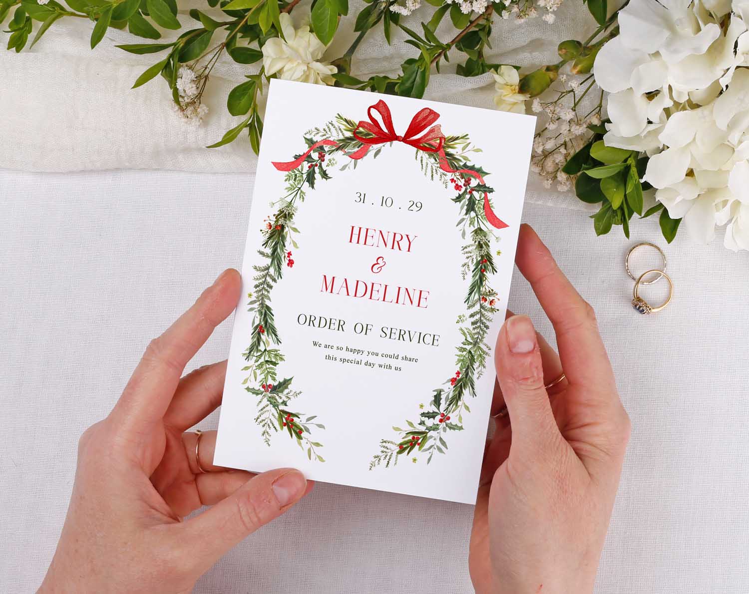 Winter Order Of Service booklet held in hands, featuring botanical design and red bow, perfect for wedding ceremony.
