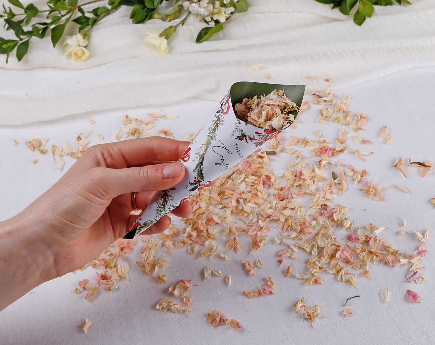 Hand holding a Winter Wedding Confetti Cones filled with petals, surrounded by confetti on a table.
